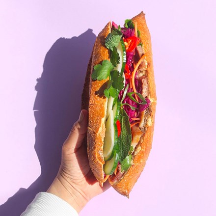 hand holding a vietnamese sandwich called banh mi on a purple background 