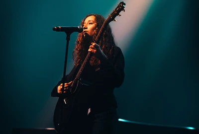 TESS GIORDANO Une photo de l'artiste Tess Giordano sur scène qui chante avec sa guitare à la main