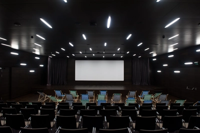 Ciné-dimanche Salle de cinéma du MEG - auditorium avec un grand écran et devant des transats et des chaises.