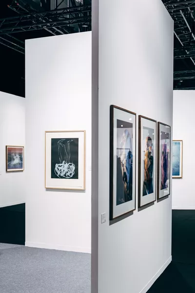 Art Genève Photographie d’un espace d’exposition d’art contemporain, avec plusieurs œuvres encadrées accrochées à de grandes cloisons blanches, sous une structure métallique noire.