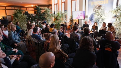 Un public assis face à 5 conférenciers.
