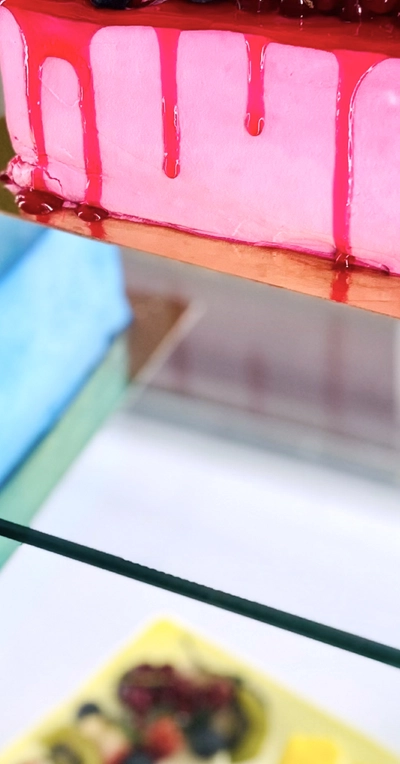 C'est un part de gateau sur une vitrine. Avec un coulis de fruits rouge, le gateau est rose.