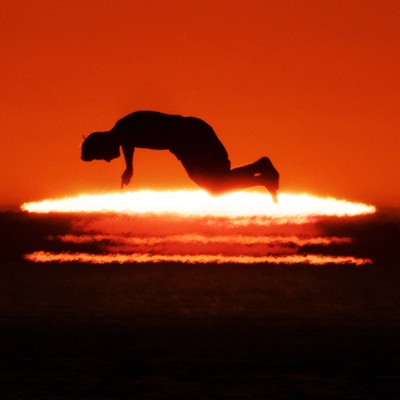 Photo contemporaine d’un coucher de soleil avec la silhouette d’un homme sautant parallèlement au soleil dans la pénombre.