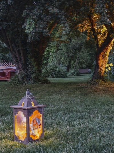 Une lanterne posée sur l'herbe et deux arbres et un fauteuil au 2ème plan
