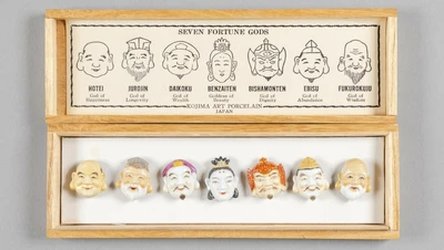 Une boîte en bois dans laquelle se trouve des boutons représentant les visages de dieux japonais.