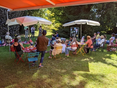Tables rondes et chaises avec des parasols disposées dans le jardin. Des gens écoutant des orateurs