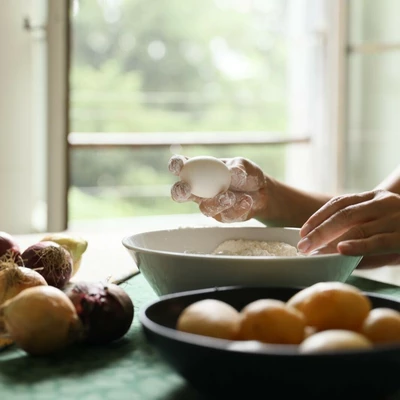 Plan serré sur des mains en train de casser un œuf dans un bol rempli de farines