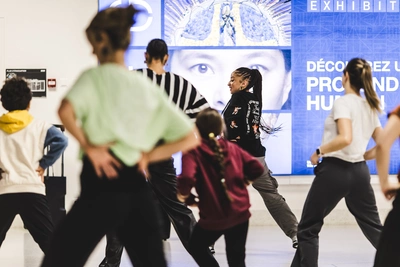 Afrosonica - Soundscapes. Fusion dance workshop Azonto and Amapiano Photo d'un cours de danse au MEG. La professeurs et de côté et les participant-e-s de dos. Il y a des enfants et des adultes qui participent.