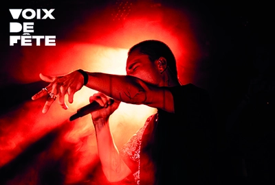 Une image de Piotr en train de chanter sur scène avec un éclairage rouge, tenant le micro dans sa main droite, le bras gauche tendu