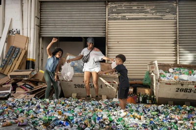 FILMAR Screenings – A melhor mãe do mundo, as part of the November 25 Campaign - Geneva. Une mère et ses enfants sautent en souriant dans un tas de déchets (des canettes vides)