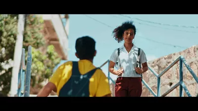 Une fille marche en souriant, un garçon est de dos et avance face à elle