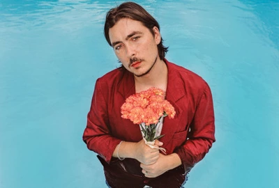 C'est une image en couleur de l'artiste qui est dans une piscine et tient un bouquet de fleur.