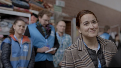 Une femme sourit à une personne hors cadre, devant un stand d'aide humanitaire.
