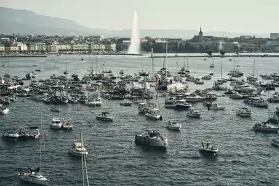 ON THE WATER GENEVA FESTIVAL 2026 Une foule impressionnante de bateaux est rassemblée sur le lac Léman lors de l'événement On The Water Geneva Festival. En arrière-plan, on observe le Jet d'eau de Genève, avec une vue sur la ville, la cathédrale et un aperçu du Salève