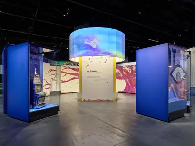 MEG X Les Créatives : The future from a child’s perspective: is it possible to exhibit without dominating? Prise de vue de l'exposition Le futur c'est quoi, on y voit au centre une projection en forme de rond sur une structure droite et sur les côtés des vitrines avec des objets.