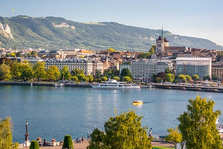 Daytime view of Geneva's lakeside old town with St. Peter's Cathedral, boats on Lake Geneva and Mont Salève in the background
