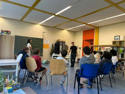 Anti-racism speech for 6 to 8-year-olds Image d'un atelier avec des enfants en rond assis sur des chaises face à un intervenant.