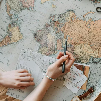 Une personne tient un stylo au dessus d'une carte du monde ouverte