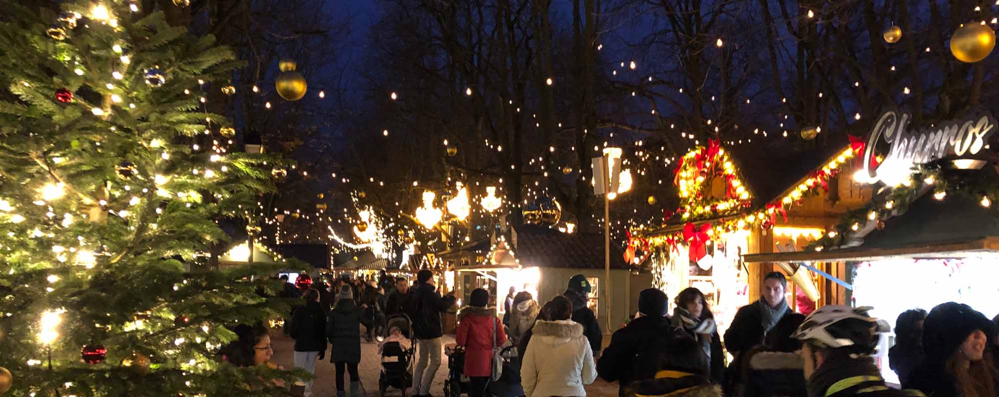 People enjoying a festive outdoor Christmas market at night with lights and decorations.
