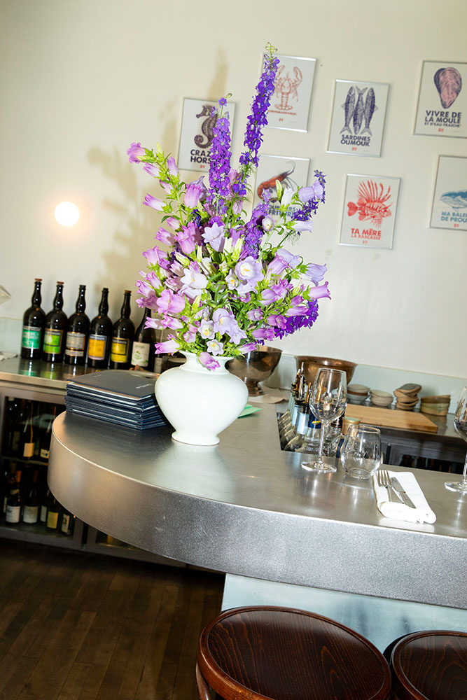 Table dressée avec un vase de fleurs violettes, des bouteilles de vin et des verres dans un restaurant