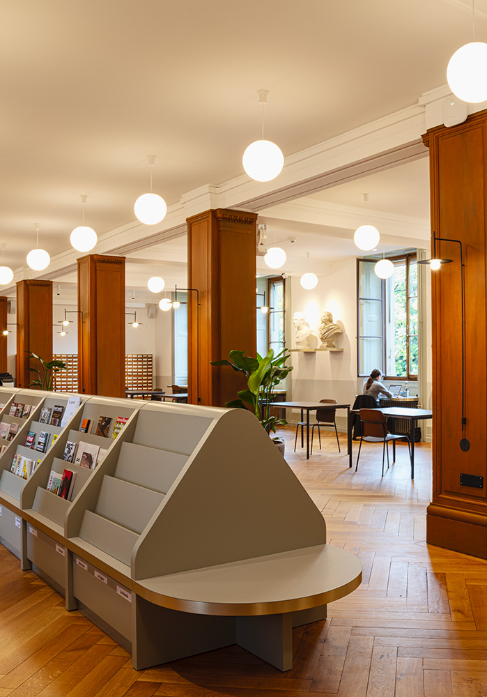Salle de lecture aux piliers en bois et luminaires suspendus à la Bibliothèque de Genève
