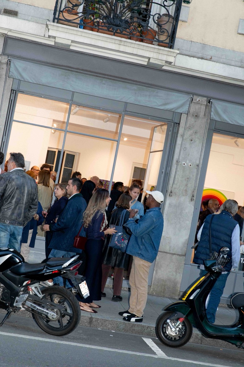Foule rassemblée devant l'entrée illuminée d'une galerie lors d'un vernissage en soirée