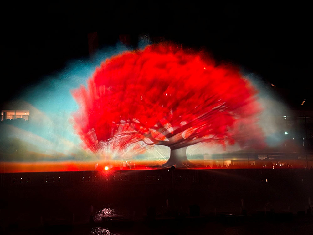 A giant illuminated tree projected onto a water screen above Lake Geneva at night